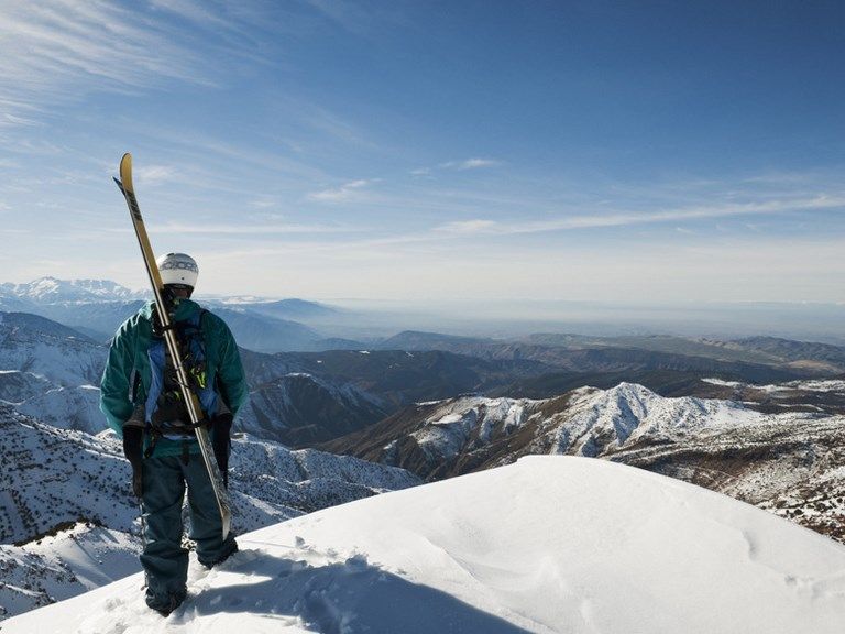 Skieur skis à l’épaule au sommet d’une crête enneigée, face aux reliefs du Haut Atlas à l’Oukaïmeden